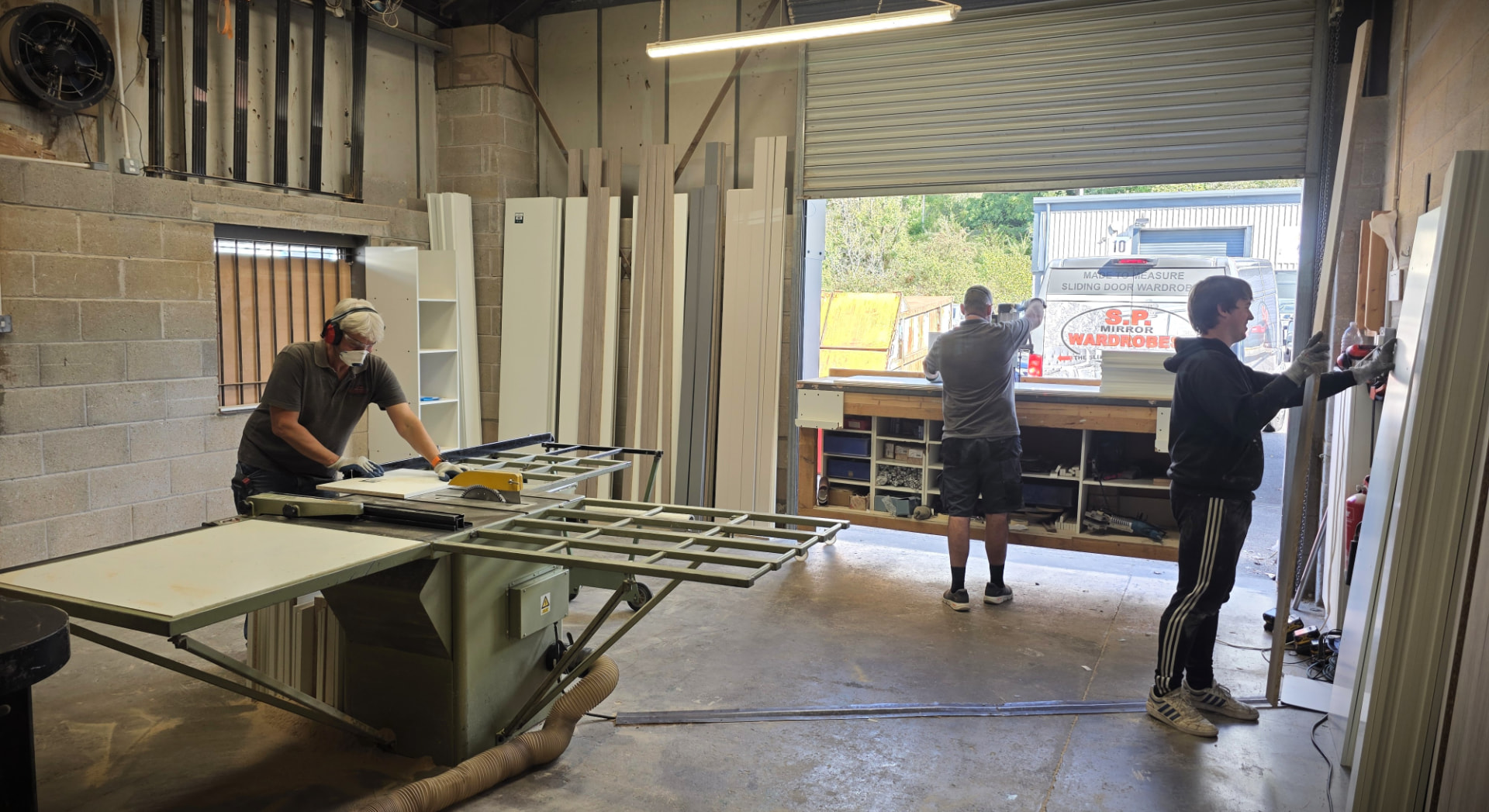 Three fitters working in the SP Mirror Wardrobes workshop in Pontypridd, with the branded van outside the shutter