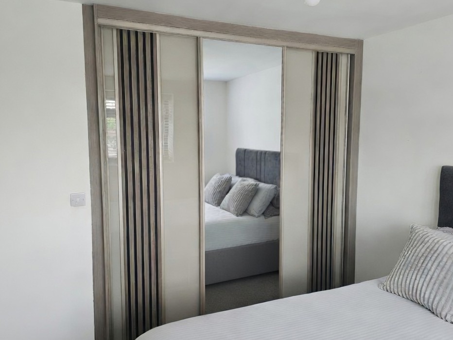Coloured glass sliding wardrobe doors with vertical acoustic wooden panels fitted in a South Wales bedroom
